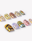 Angled flat lay of Golden Muse gold, opal, pink and green statement press-on nails with raised jeweled details
