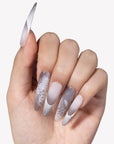 Hand model wearing Himalayan Mist press-on nails with gray lilac mist gradient, white French tips, silver crackle lines, and lace-like texture