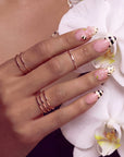 Pink press-on nails with bee-inspired stripes, polka dots, and floral accents arranged in a set layout