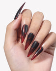White background hand model wearing Inferno Veins stiletto press-on nails with translucent red tips, black curved panels, and glossy finish