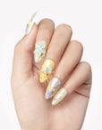 Hand close-up wearing Iridescent Petals pastel press-on nails with raised blue and pink flowers, pearls and gems