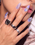 Face close-up of a model wearing Iris Bloom iridescent purple nails with raised blue flowers and pearl accents