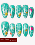 Turquoise glitter almond press-on nails with yellow and pink floral accents arranged in a flat lay