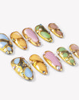 Angled flat lay of Jewel Mosaic press-on nails with blue, yellow, pink, green, and taupe panels framed in gold