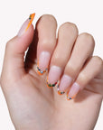 Close-up of a hand model wearing Jewel Sunset press-on nails with ruby red tips and multicolor gem accents