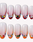 Flat lay of Jewel Sunset press-on nail swatches with soft pink bases, ruby red tips, and multicolor gem accents