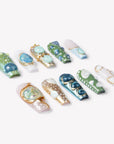 Angled flat lay of Jungle Relic green, blue, ivory and gold press-on nails with dimensional gem accents