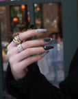 Hand model wearing Lace & Pearls press-on nails with black matte tips, white lace pattern accents, pearl trim, and statement rings