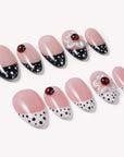 Angled flat lay of Ladybug Garden press-on nails with pink bases, black and white polka dot French tips, red ladybugs, and white flower charms