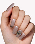Hand model wearing metallic taupe press-on nails with a gemstone accent