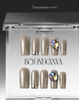 Packaging display of champagne metallic press-on nails with gemstone accents in a clear box