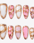 Liquid Gold pink and white press-on nails with raised rose gold frames and crystal accents in a flat lay