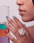 Hand model wearing Liquid Mercury press-on nails with silver chrome swirls, blue gray French tips, and glossy red accents