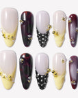 Lunar Velvet press-on nails with pale yellow tips, black dotted lattice designs, burgundy cat eye polish, gold beads, pearls, and glossy nude bases