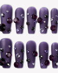 Flat lay of Luxurious Treasure press-on nails in a muted purple square style with dark purple, black, and clear rhinestone gems