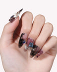 Hand model wearing Mineral Dreamscape press-on nails with lilac, black, and silver tones and gemstone accents