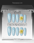 Press-on nails displayed in a clear BeyondCanva case with light blue polka dot nails and yellow flower accents.