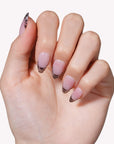Close-up of a hand model wearing Mist Fade press-on nails in nude gray with soft white smoky tips
