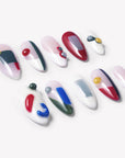 Flat lay of Modernist Dream press-on nails with abstract red blue yellow green color blocks, raised round accents, and glossy nude white bases