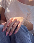 Nebula Kiss purple and pink cat-eye press-on nails with glowing hearts shown on a hand model wearing blue jeans