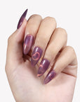 Close-up hand model wearing Nebula Kiss purple and pink cat-eye almond press-on nails with glowing heart accents