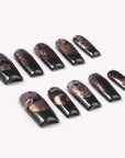 Nocturne Gild press-on nails in glossy black with metallic gold foil accents arranged in a flat lay on a white background