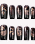 Nocturne Gild press-on nails in glossy black with metallic gold foil accents arranged on a white background