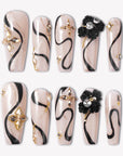 Flat lay of beige press-on nails with black swirls, gold accents, and floral embellishments.
