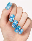 Close-up of a hand wearing blue rhinestone press-on nails on a white background.