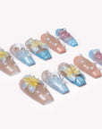 A flat lay of beach-inspired press-on nails with yellow flowers, starfish accents, and pearl details on a white background