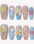 A set of beach-inspired press-on nails with yellow flowers, starfish accents, and pearl details on a white background
