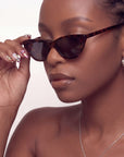 Lifestyle portrait of a hand model wearing Opulent Ribbon Reverie press-on nails while adjusting sunglasses