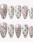 Parisian Polka press-on nail set in ivory and blush with black polka dots and pearl chain accents arranged on a white background