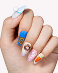 Hand model wearing cartoon-themed press-on nails with blue, white, pink, and orange character-inspired accents