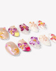 Angled flat lay of Petal Poem colorful press-on nails with sculpted purple, pink, peach and yellow flowers