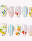 Set of handmade press-on nails with fruit and floral designs, blue stripes, and pastel accents on a white flat lay.