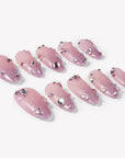 Angled flat lay of Pink Fairy Dust press-on nails with soft pink shimmer, glittery cat-eye tips, and rhinestone accents