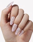Hand model wearing blush pink press-on nails with black and silver polka dots