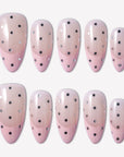 Flat lay of blush pink and beige press-on nails with black and silver polka dots in rounded oval shapes