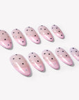Flat lay of blush pink press-on nails with black polka dots and glossy pink French tips