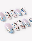 Angled flat lay of Retro Pastoral press-on nails with pale pink bases, light blue curved tips, gold foil accents, and red and blue floral designs