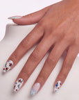 Hand model wearing Retro Pastoral press-on nails with pale pink bases, light blue curved tips, gold foil accents, and tiny floral designs