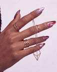 Rose Drift burgundy and pink cat eye almond press-on nails shown on a hand model with rings and a pendant
