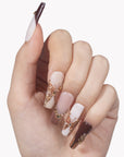 White background hand model wearing Rosegold Flutter press-on nails with burgundy tips, soft pink accents, rosegold butterfly charms, and rhinestones