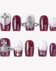Royal Rebellion press-on nails with red black argyle pattern, white gradient bases, silver orb charms, cross charm, pearls, and rhinestones