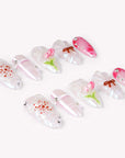 Angled flat lay of Sakura Whisper pearly white and pink press-on nails with blossoms, tulips, bows, plaid and silver studs