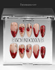 Scarlet Heart Oath press-on nails displayed in clear packaging with nude, deep red, and gold heart, starburst, and bead accents