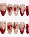 Scarlet Heart Oath press-on nails in nude, deep red, and gold with heart and starburst accents arranged in a flat lay