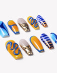 Angled flat lay of Solar Tide press-on nails with blue and orange wave art, striped accents, and metallic gold marbling