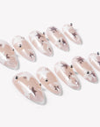 Flat lay of Starlit Whisper press-on nails with translucent nude pink bases, white star patterns, silver star accents, silver beads, and glossy almond shapes